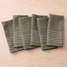 four linen napkins with white stripes on them sitting on a wooden table top next to each other