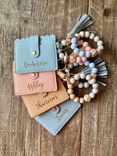 three personalized leather keychains with tassels and charms on top of a wooden table