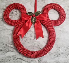 a mickey mouse ornament with red beads and a bow hanging on a wall