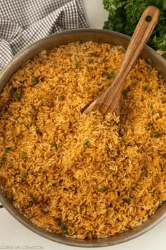 a pan filled with rice and parsley on top of a counter next to a wooden spoon