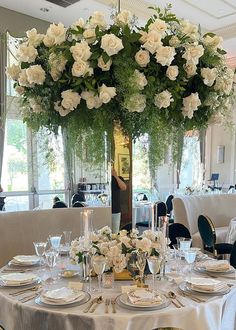 a table set with white flowers and place settings in a fancy dining room at a restaurant