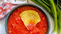 a bowl of salsa with a tortilla chip in it next to green onions