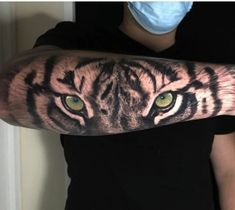 a person wearing a face mask with a tiger tattoo on their arm and the eyes are green