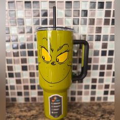 the grin face on this green travel mug is drawn with yellow eyes and has a black handle