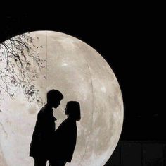 two people standing next to each other in front of a full moon