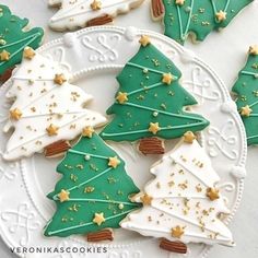 decorated christmas cookies on a white plate with gold stars and green frosted trees in the middle