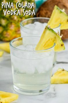 two glasses filled with ice and some pineapples in the background on a table