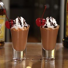 two glasses filled with ice cream, chocolate and cherries on top of a table