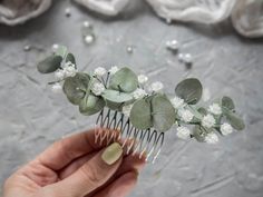 a hand holding a hair comb with flowers and leaves on top of it in front of a gray background