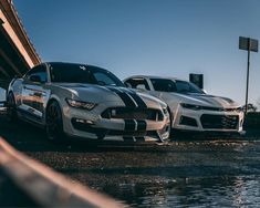 two cars parked next to each other in front of a bridge with water on the ground