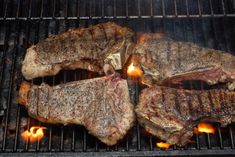 three steaks cooking on the grill with flames