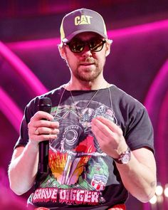 a man wearing sunglasses and a hat holding a microphone in front of his face while standing on stage