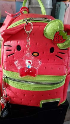 a pink and green hello kitty backpack with a cat face on the front, attached to a keychain