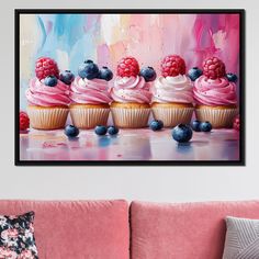 three cupcakes with raspberries and blueberries on them are sitting in front of a pink couch