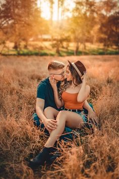 a man and woman sitting on the ground kissing in a field with tall brown grass