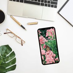 a cell phone sitting on top of a white desk next to a laptop and glasses