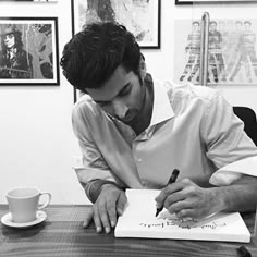 a man sitting at a table writing on a piece of paper with a pen in his hand