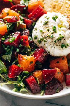 a white plate topped with salad and fried egg next to bread on a marble table