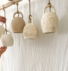 three hanging tea kettles with one being held by a woman's hand and the other is holding a cup