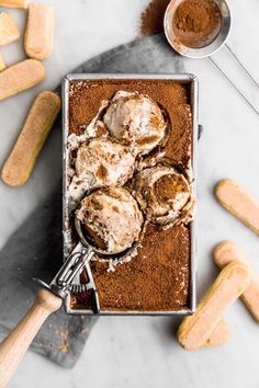 a pan filled with ice cream on top of a counter next to cookies and spoons