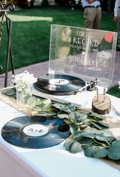 a record player on top of a table with flowers and greenery next to it