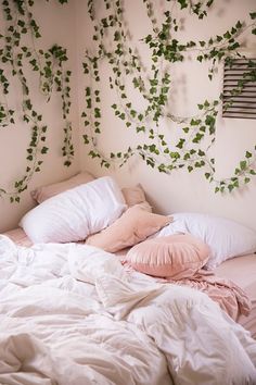 an unmade bed with white sheets and pink pillows in front of ivy covered wall