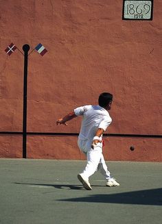 a man in white is playing tennis on a court with a red wall behind him