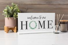 a welcome to our home sign next to a potted plant and candle holder on a table