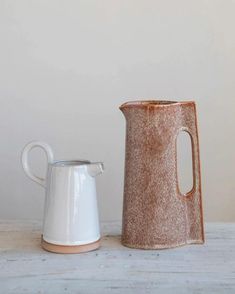 two white and brown vases sitting next to each other on top of a table