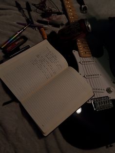 an open notebook sitting on top of a bed next to a guitar and other musical instruments