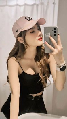 a woman taking a selfie in front of a mirror wearing a hat and holding a cell phone