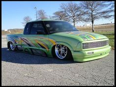 a green truck with colorful stripes painted on it's hood parked in a parking lot