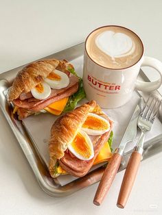 two sandwiches on a tray next to a cup of cappuccino and utensils