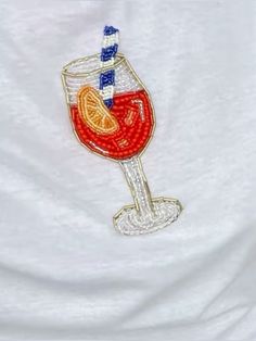 a white t - shirt with a red wine glass and orange slice embroidered on it