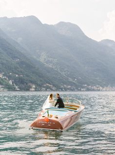 two people in a boat on the water with mountains in the backgrouds