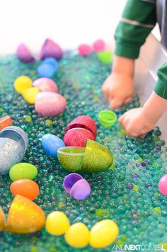 a child is playing with colored rocks and plastic eggs on the floor in an indoor play area