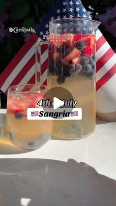 a pitcher filled with fruit sitting on top of a table next to two glasses and an american flag