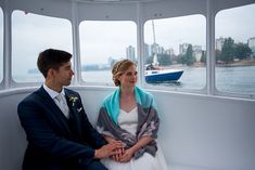 a man and woman sitting on a boat looking out the window at the water with boats in the background