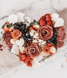 a heart shaped platter filled with fruit and cheese on top of a marble table