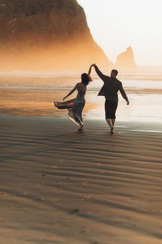 two people are dancing on the beach near the water's edge in front of an ocean cliff