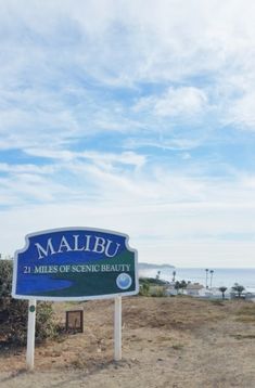 a blue sign sitting on top of a dry grass covered field next to the ocean