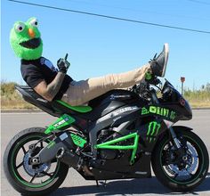 a man sitting on top of a motorcycle wearing a green sesame character hat and sunglasses