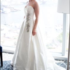 a woman in a white wedding dress standing next to a window looking at the camera