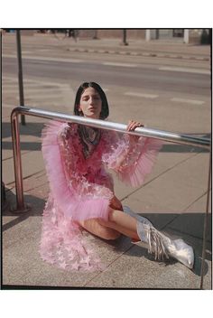 a woman in a pink dress sitting on the sidewalk