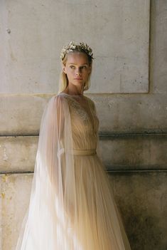 a woman in a wedding dress with a veil on her head standing next to a wall