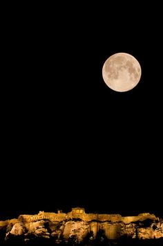 the full moon is seen over an old castle on top of a hill at night