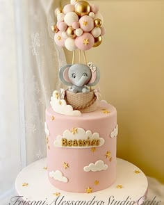 a pink and gold baby shower cake with an elephant sitting on it's top