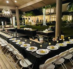 a long table set up with white plates and silverware for an outdoor dinner party