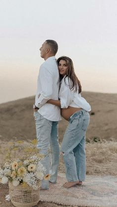 a man and woman standing next to each other on top of a blanket in the desert