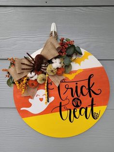 a trick or treat sign hanging on the side of a wooden wall with pumpkins and leaves